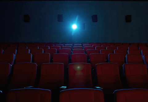 Interior of movie theater with empty red seats and projector